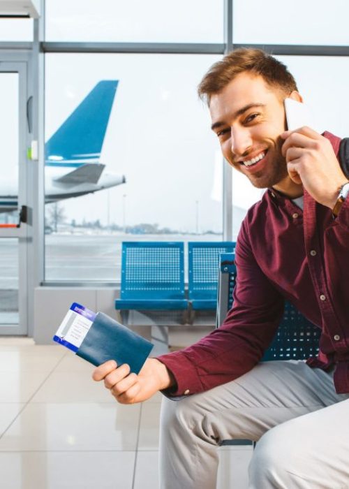 smiling-man-talking-on-smartphone-while-sitting-in-airport-with-backpack-e1695641625767